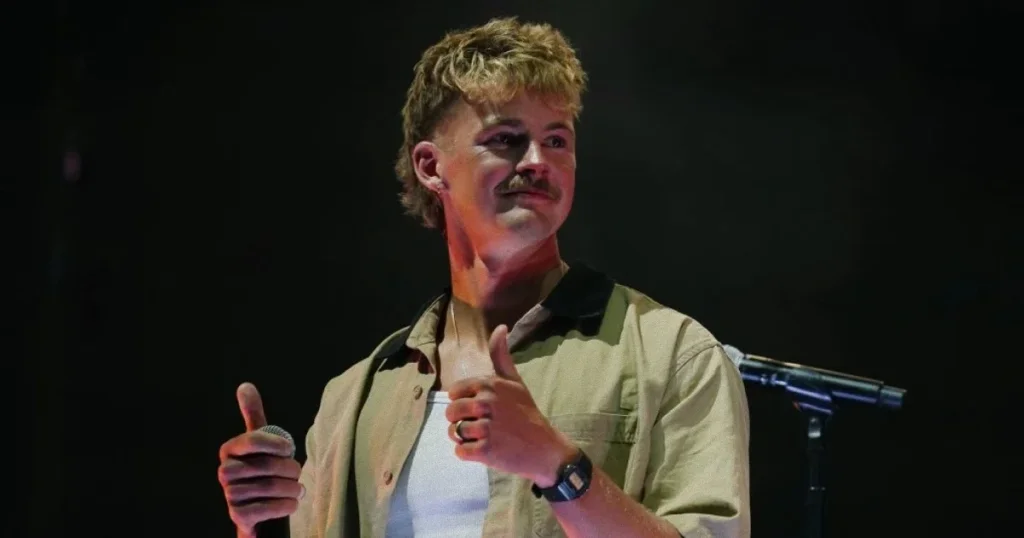 Imagen de Forrest Frank en el escenario de UniteUS con las manos levantadas, audiencia de fondo, iluminación dramática que capture el momento emotivo del testimonio