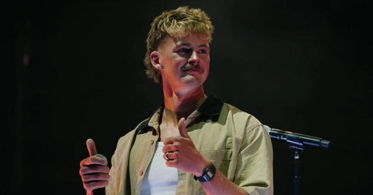 Imagen de Forrest Frank en el escenario de UniteUS con las manos levantadas, audiencia de fondo, iluminación dramática que capture el momento emotivo del testimonio